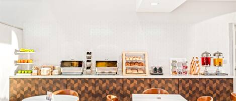 Una cocina moderna con salpicadero de ladrillo blanco, encimera de madera con patrón de espiga y barra de desayuno con diferentes alimentos y electrodomésticos.