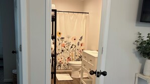 A bathroom with a shower curtain, toilet, and a small white cabinet.