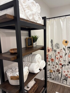 A multi-tiered wooden shelf unit with towels, a framed inspirational quote, a potted plant, and a basket. - Affordable Luxury / Quiet / 2 min to Erskine College & The Renaissance (Donalds)