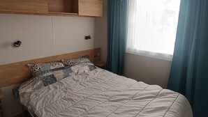 Une chambre à coucher avec un lit, une tête de lit en bois, une fenêtre avec des rideaux et une étagère fixée au mur.