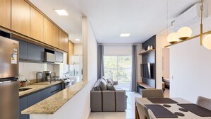 Una cocina moderna con electrodomésticos integrados, un comedor con mesa y sillas, y una sala de estar con sofá y televisor.