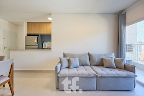A modern living room with a grey sofa, wooden cabinets, and a window with a view. - Beautiful Apartment on Toninhas Beach - REF LY06H (Ubatuba)