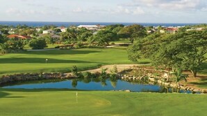 A golf course with a pond, surrounded by greenery and houses in the background. - 4-bedroom villa in wonderful Oistins with pool (Oistins)