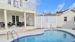 A swimming pool with a white deck, a covered seating area, and a building with a balcony. - 4-bedroom villa in wonderful Oistins with pool (Oistins)