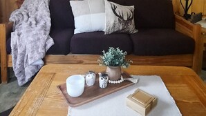 En hyggelig stue med trægulv, en mørk sofa med dekorative puder, et træ sofabord med en underlag og et spejl på væggen.