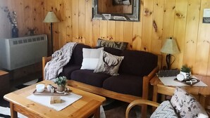 En hyggelig stue med trævægge, en mørk sofa, et træ sofabord, en blomstret lænestol og en loftsvifte.