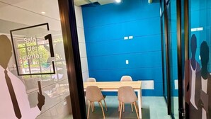 A conference room with a blue accent wall, a glass partition, and a wooden table with chairs. - 605-Estudio luminoso con balcón  (Bogotá)