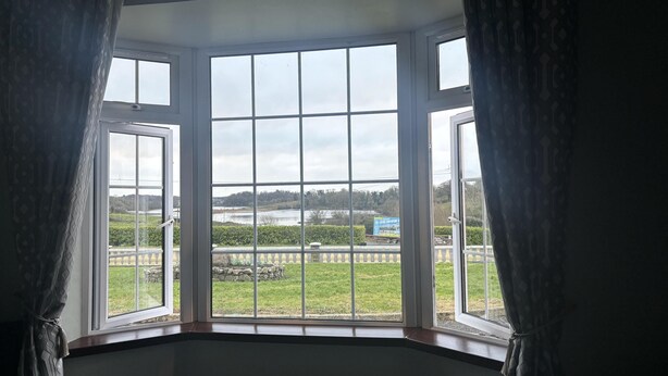 Ein Zimmer mit Erkerfenster mit Blick auf eine Wiese und ein Gewässer.