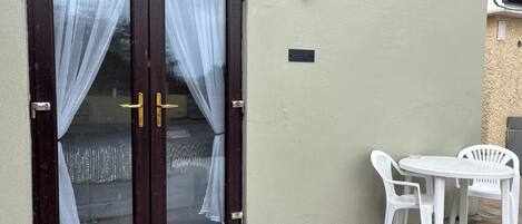 A double door with curtains, a small outdoor table with chairs, and a wall-mounted light fixture.