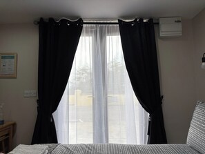 A room with a bed, a window with curtains, an air conditioning unit, and a wall-mounted light fixture. - Private Small Detached Room With Bathroom (Cavan)