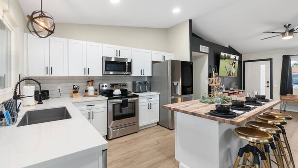 A modern kitchen with white cabinets, stainless steel appliances, a central island with stools, and a ceiling fan. - Heated Pool + Hot Tub | Backyard Resort | Games (Mesa)