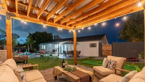 An outdoor patio with wooden beams, a dining area, and a pool. - Heated Pool + Hot Tub | Backyard Resort | Games (Mesa)