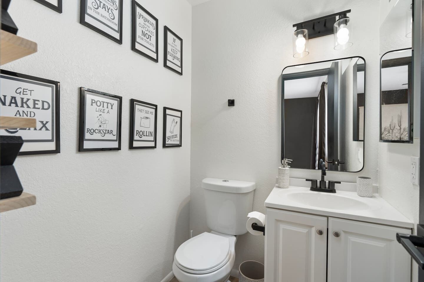 A bathroom with a toilet, sink, and mirror. There are framed quotes on the wall.