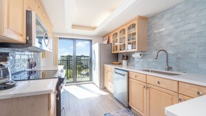 A modern kitchen with wooden cabinets, a stainless steel range hood, a built-in dishwasher, and a large window providing a view of the outdoors. - Beachfront Bliss: 2-Bed/2-Bath Condo with Stunning Views! (Fort Myers Beach)