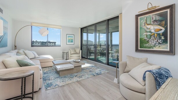 A modern living room with a sofa, armchairs, a coffee table, and a large window offering a view of the sea. - Beachfront Bliss: 2-Bed/2-Bath Condo with Stunning Views! (Fort Myers Beach)