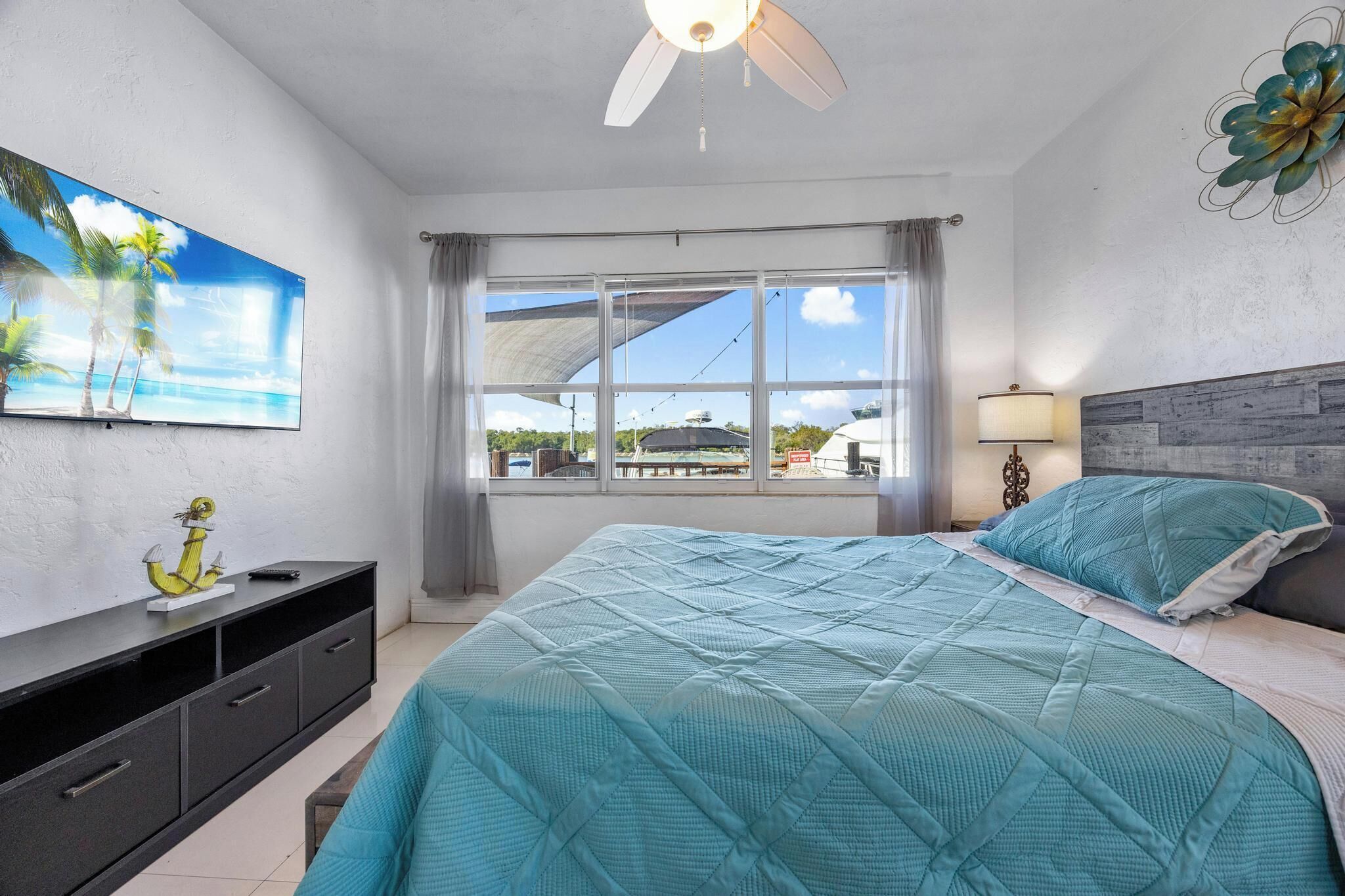 Ein Schlafzimmer mit einem Bett, einem Fernseher, einem Nachttisch und einem Fenster mit Blick ins Freie.