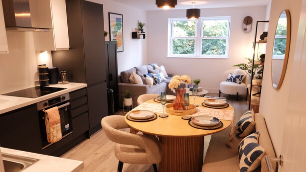 A modern kitchen with a dining area, featuring a round wooden table, beige chairs, and a sofa with patterned cushions. - Stylish, Luxury Apartment Sleeps 4 - Southampton (Southampton)