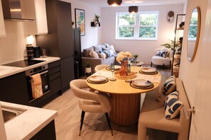 Una cocina moderna con zona de comedor, que incluye una mesa redonda de madera, sillas color beige y un sofá con cojines estampados.