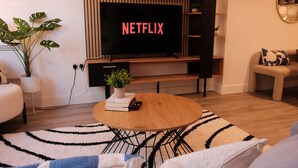 A living room with a wooden coffee table, a TV displaying 'NETFLIX', a potted plant, and a bookshelf. - Stylish, Luxury Apartment Sleeps 4 - Southampton (Southampton)