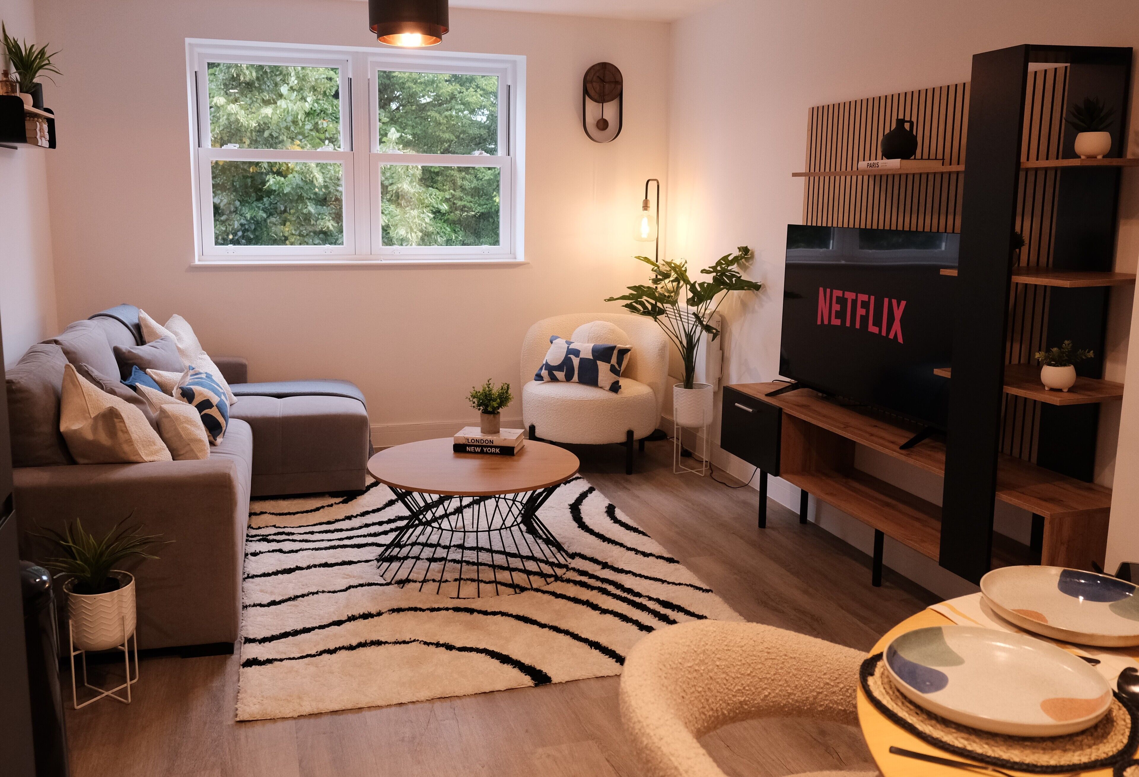 En moderne stue med sofa, lænestol, sofabord og fjernsyn på et træstel.