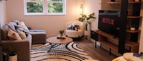 A modern living room with a sofa, armchair, coffee table, and a TV on a wooden stand.