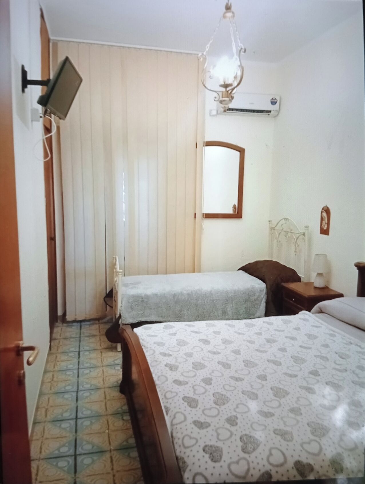 A bedroom with two beds, a ceiling fan, an air conditioning unit, a mirror, and a window with blinds.