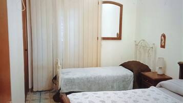 A bedroom with two beds, a ceiling fan, an air conditioning unit, a mirror, and a window with blinds.