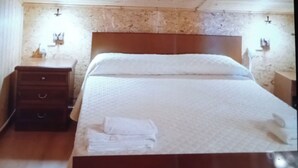 Un dormitorio con techo de madera, una cama con cubrecama blanco, una mesita de noche de madera y una pared de piedra.
