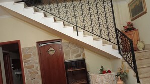 Una escalera con baranda de hierro forjado, una puerta de madera con un tragaluz en forma de diamante y una pared de piedra.