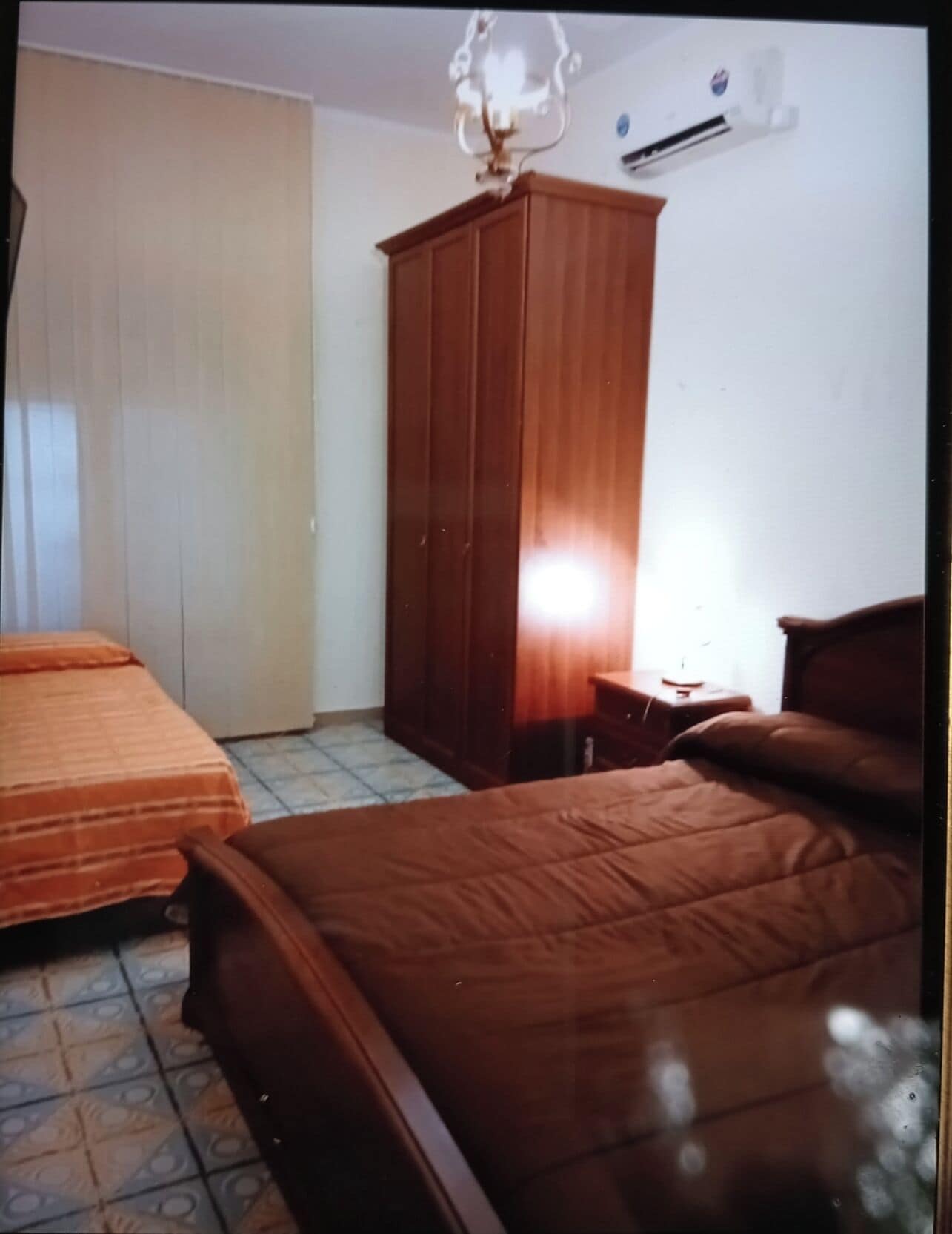 A bedroom with two beds, a wardrobe, and an air conditioning unit.