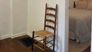 A room with a wooden chair, a bed with beige bedding, and a white wall. - 2Bed 1Bath 1930s KC Home off I-35 ~ Walking Distance to Coffee & Breakfast (Kansas City)