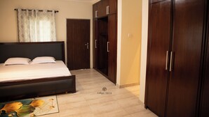 A bedroom with a bed, wardrobe, and a door leading to another room. - Unique Green Lodge (Accra)