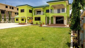 A two-story house with a green exterior, a front porch, and a well-maintained lawn. - Unique Green Lodge (Accra)