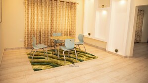 A dining area with a round table, four chairs, a patterned curtain, and a green rug. - Unique Green Lodge (Accra)