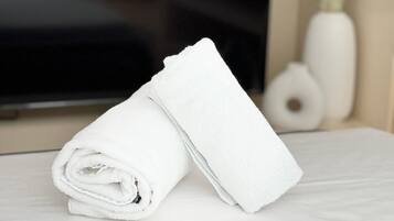A neatly folded white towel on a bed with a television displaying the word "FLIX" in the background.