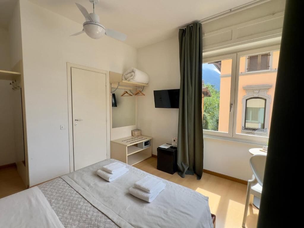 Habitación de hotel con cama, escritorio, silla, televisor y ventana con cortinas.