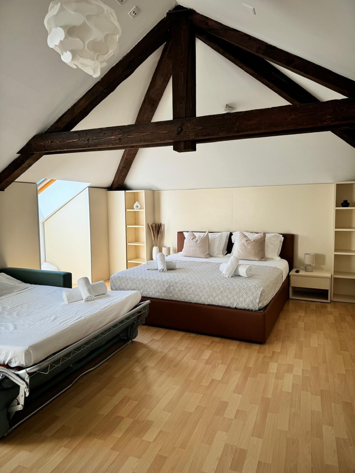 A bedroom with two beds, wooden beams, a wooden floor, and a white ceiling light fixture.