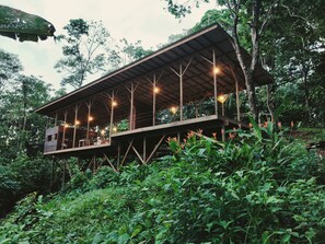 Una estructura de madera con balcón, rodeada de abundante vegetación.