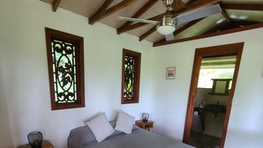 Un dormitorio con una cama de madera, dos mesitas de noche, un ventilador de techo y dos ventanas decorativas.