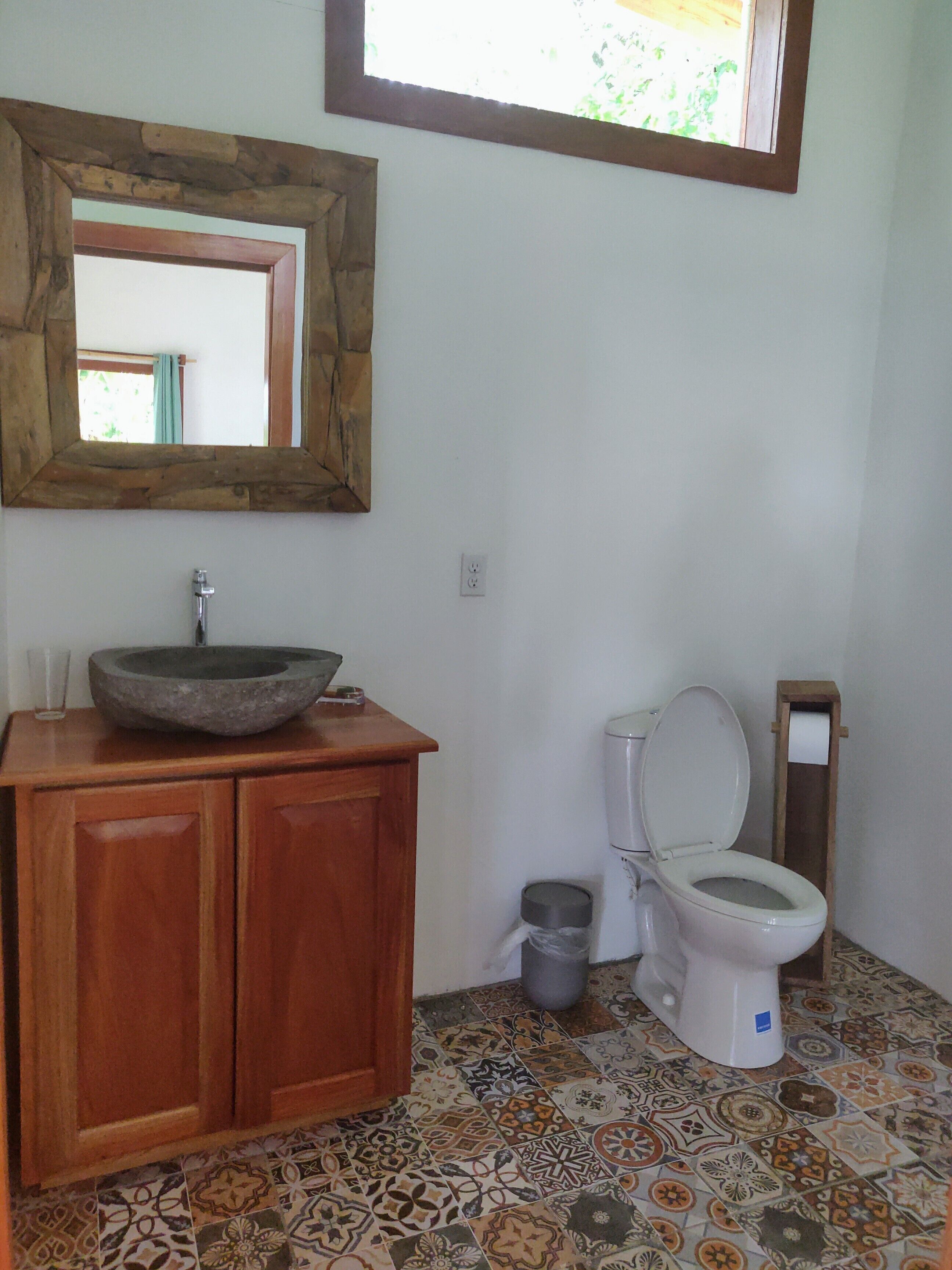 Un baño con lavamanos de piedra, armarios de madera, inodoro y baldosas de suelo con diseño.