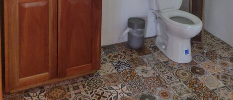 Un baño con lavamanos de piedra, armarios de madera, inodoro y baldosas de suelo con diseño.