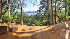 Terraza de madera con mobiliario de mimbre y una hamaca con vista a un lago.