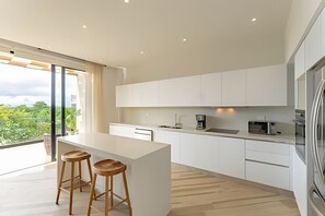 A modern kitchen with a large island, white cabinets, and stainless steel appliances. There are two wooden stools at the island. - oasis yaaxlum (Tulum)