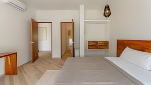 A modern bedroom with a large bed, wooden headboard, and a hanging light fixture. - oasis yaaxlum (Tulum)