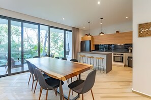Eine moderne Küche mit Holzschränken, einer zentralen Kochinsel mit Barhocker und großen Fenstern mit Blick auf Grünflächen.