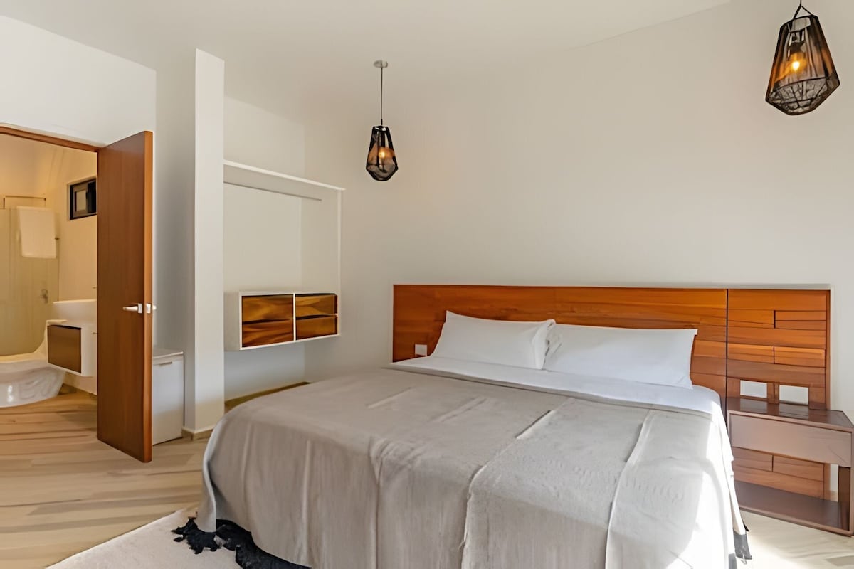 A bedroom with a wooden headboard, a large bed with white bedding, a bedside table, and two pendant lights.