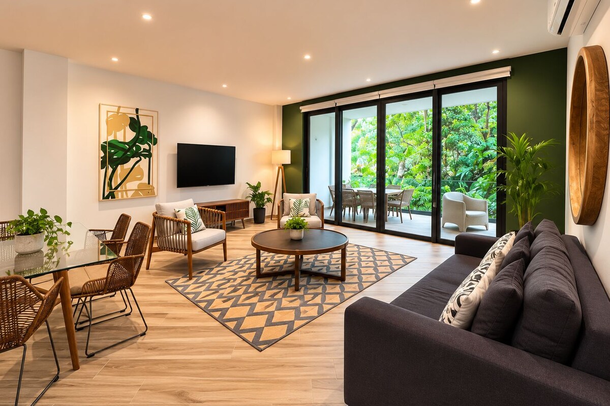 A modern living room with a sofa, chairs, a coffee table, and a TV. There is a large window with a view of greenery outside.