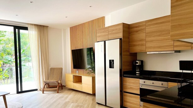A modern kitchen with wooden cabinetry, a built-in TV, and a black countertop. - oasis yaaxlum (Tulum)