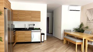 A modern kitchen with wooden cabinets, a stainless steel refrigerator, and a dishwasher. There is a dining area with a wooden table and benches. - oasis yaaxlum (Tulum)