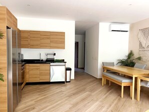 A modern kitchen with wooden cabinets, a stainless steel refrigerator, and a dishwasher. There is a dining area with a wooden table and benches. - oasis yaaxlum (Tulum)